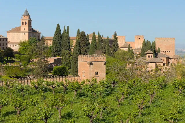 The towers and walls of the Alhambra rising above green terraced gardens and cypress trees seen from the Generalife