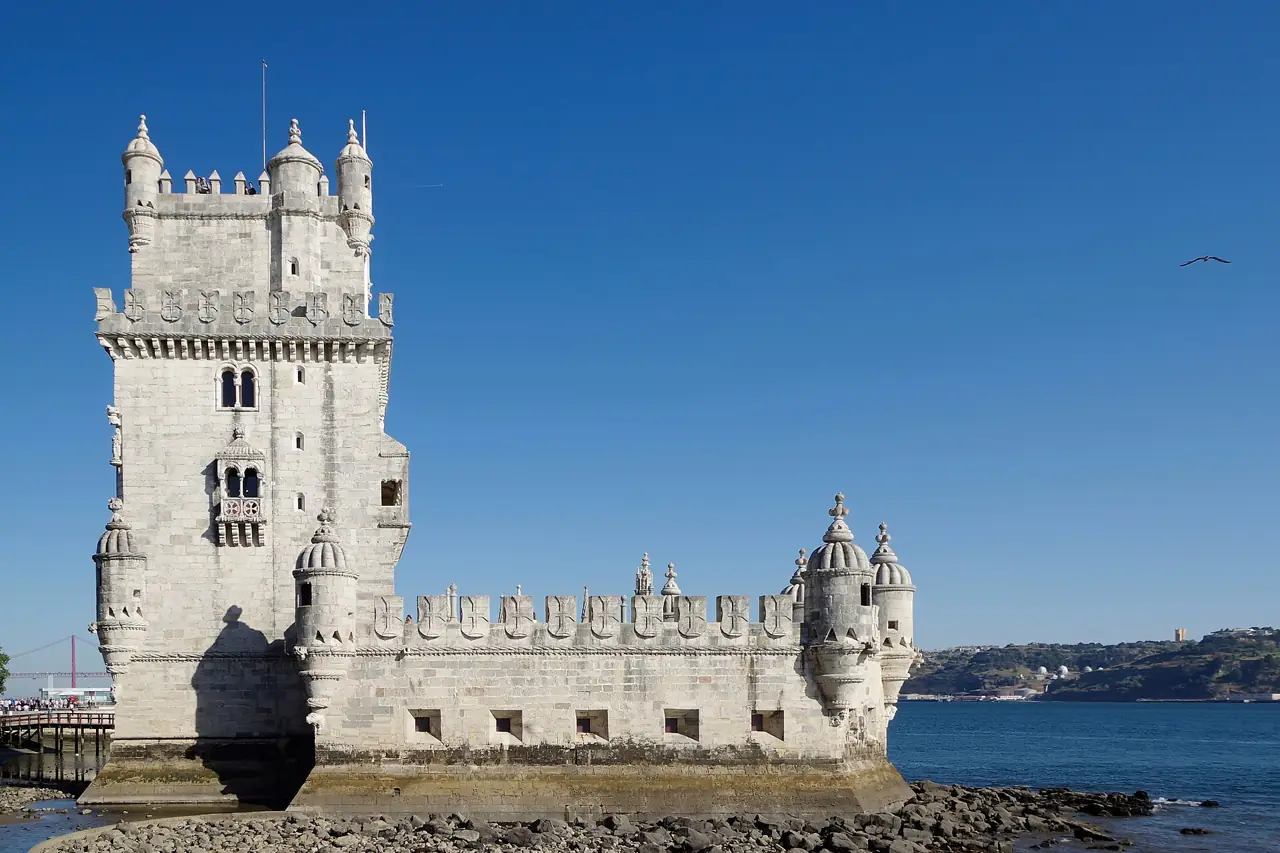 The white stone Belém Tower standing at the edge of the Tagus river under a deep blue sky