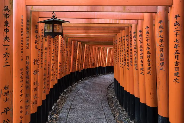 A stone path through a tunnel of inscribed vermilion torii gates, with a hanging lantern, at Fushimi Inari Shrine