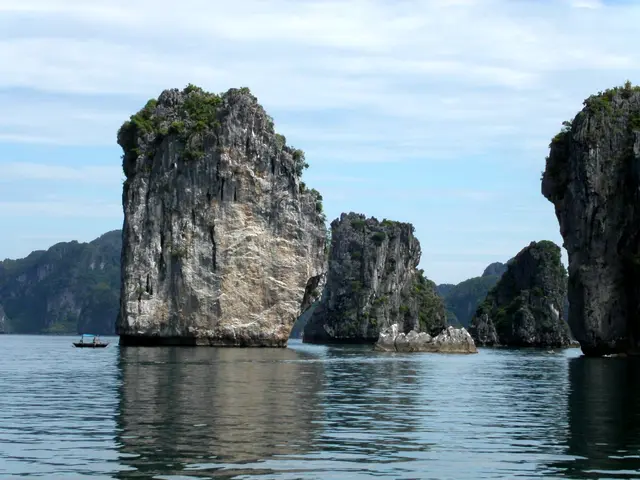 Sheer limestone islets rising from calm water in Ha Long Bay, with a small fishing boat in the distance