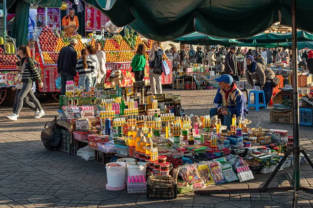 Colourful market stalls and shoppers on Jemaa el-Fna square in Marrakech under green parasols
