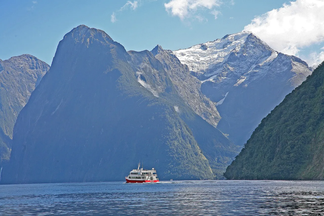 A cruise boat on Milford Sound beneath the steep peaks of Fiordland, with snow on the higher summits