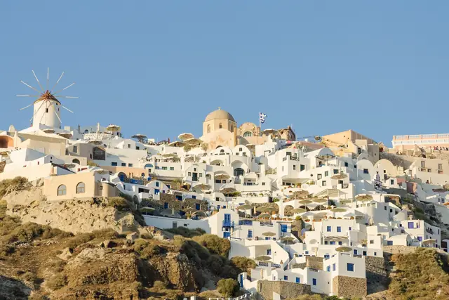 White cube houses and a windmill of Oia spread along the caldera cliff on Santorini