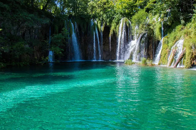Several waterfalls cascading through green forest into a clear turquoise lake at Plitvice Lakes National Park