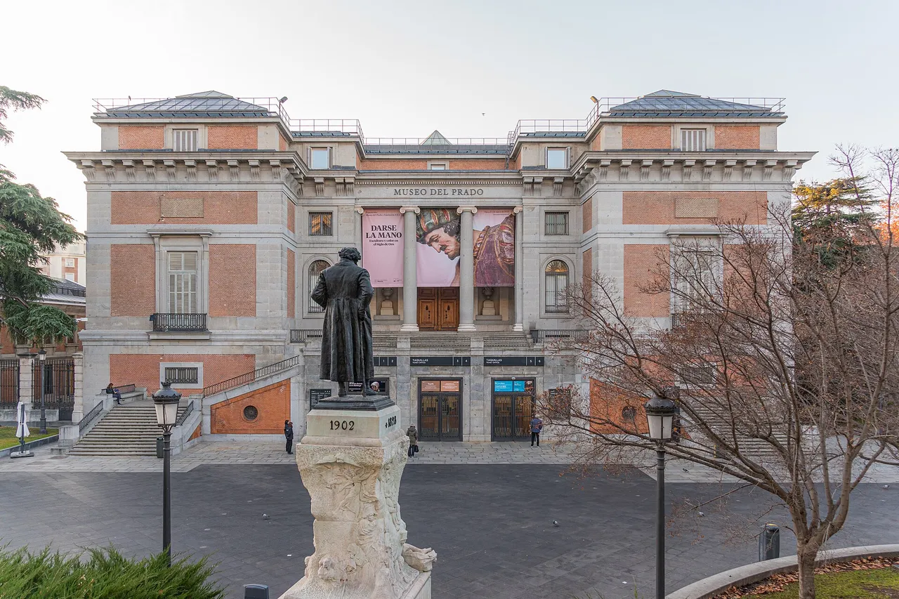The neoclassical brick and stone facade of the Prado Museum in Madrid with a statue of Goya in front