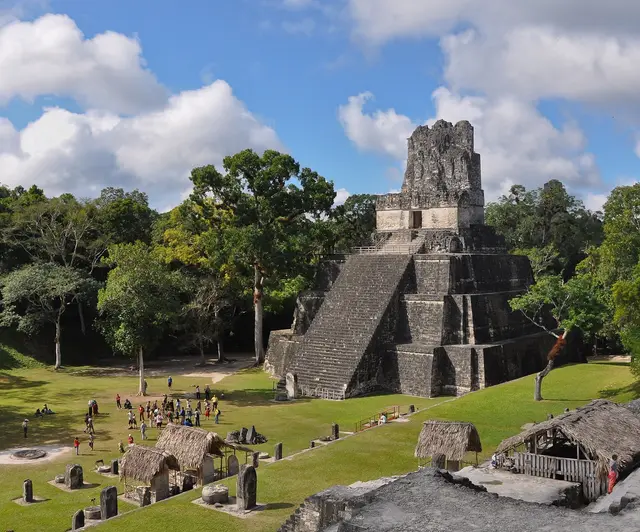 Temple II rising above the grassy Great Plaza at Tikal, surrounded by rainforest trees