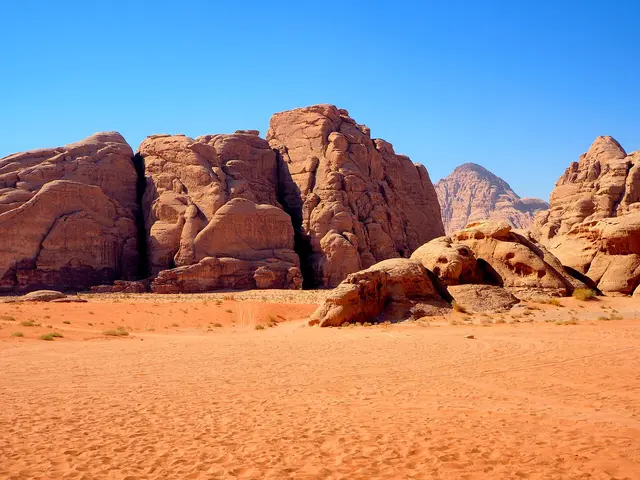 Weathered sandstone mountains rising above orange sand in the Wadi Rum desert, Jordan