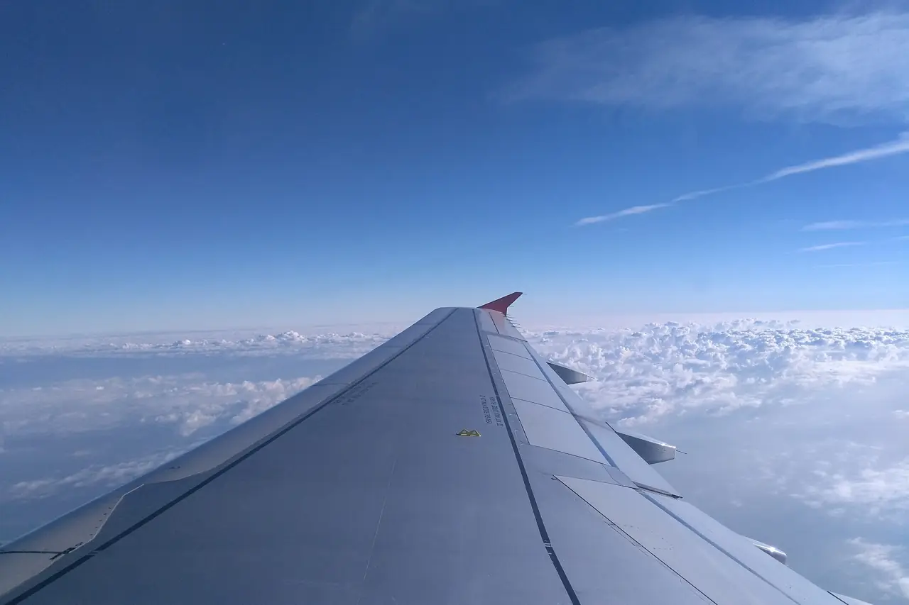 View from an aeroplane window of the wing above a layer of white clouds and blue sky