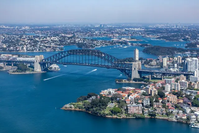 Aerial view of Sydney Harbour Bridge spanning the harbour, with the city and Kirribilli waterfront below