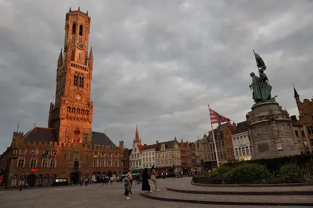 The medieval Belfry and a bronze statue on the Markt square in Bruges at dusk