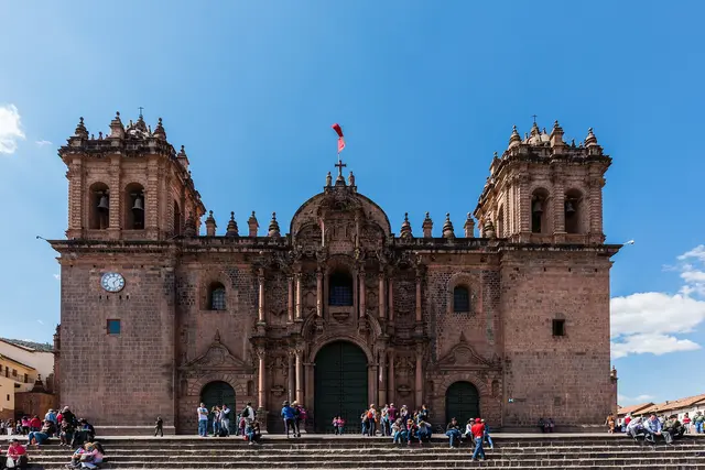 The stone cathedral on the Plaza de Armas in Cusco under a blue sky, with people on its steps