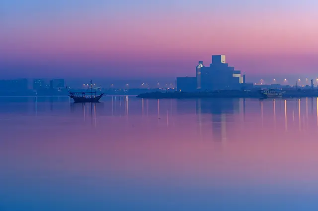 The Museum of Islamic Art and a traditional dhow silhouetted against a pink and violet dawn sky over Doha Bay