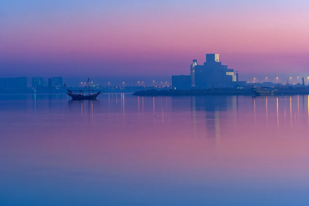The Museum of Islamic Art and a traditional dhow silhouetted against a pink and violet dawn sky over Doha Bay