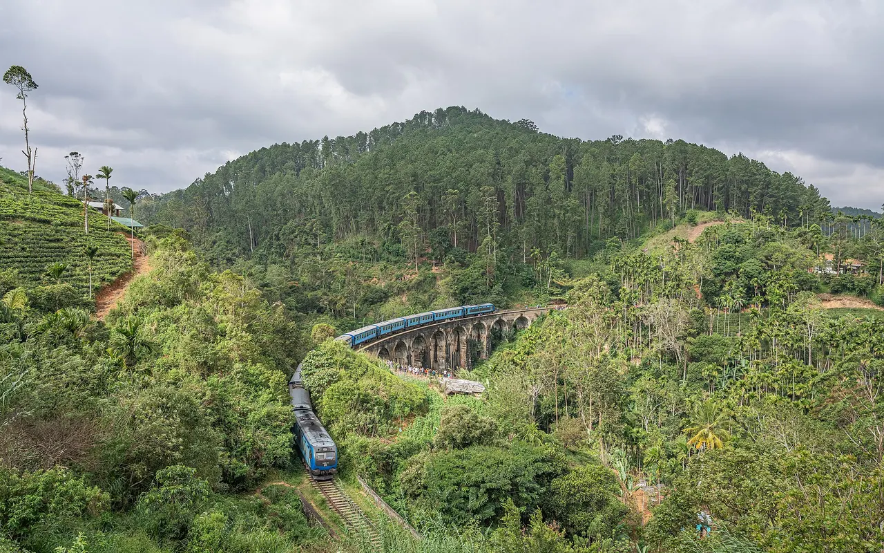 A blue train crossing the Nine Arch Bridge near Ella, surrounded by forested hills and tea plantations