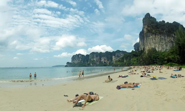 Sunbathers on the sandy beach of Railay in Krabi, Thailand, beneath towering limestone cliffs
